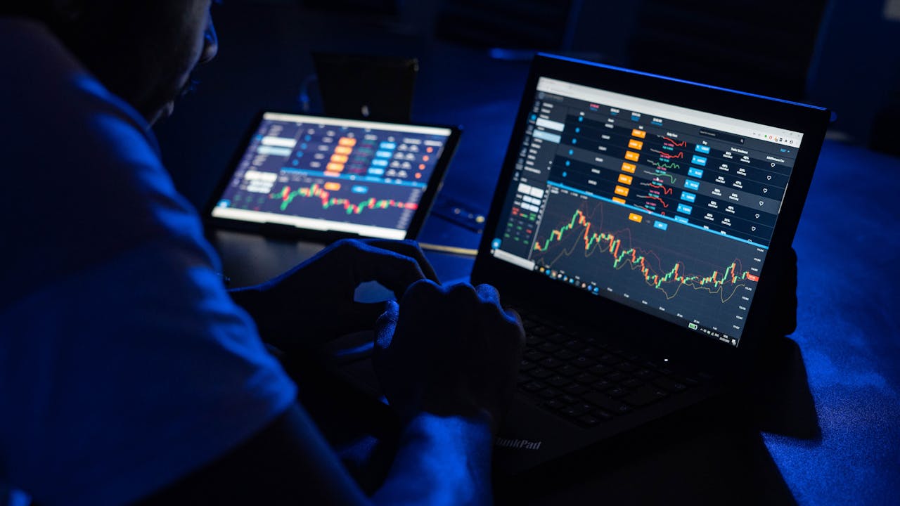 The Art of Drawing Readers In: Your attractive post title goes here Man analyzing financial charts and data on laptops in a dimly lit room, highlighting forex trading.